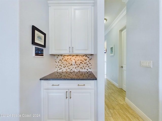 kitchen featuring light hardwood / wood-style flooring, dark stone countertops, decorative backsplash, ornamental molding, and white cabinets