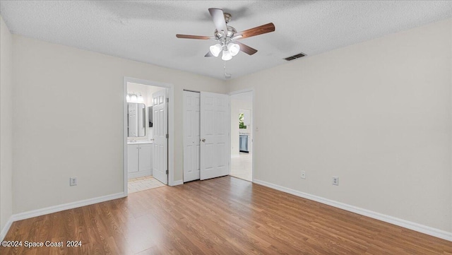 unfurnished bedroom featuring a textured ceiling, ensuite bathroom, ceiling fan, and light hardwood / wood-style flooring