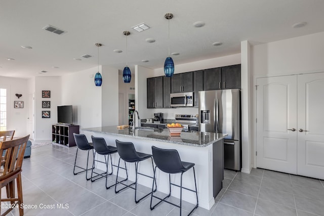 kitchen with appliances with stainless steel finishes, pendant lighting, stone counters, and a kitchen island with sink