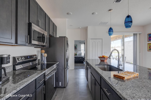 kitchen with light stone counters, sink, dark tile patterned floors, decorative light fixtures, and stainless steel appliances