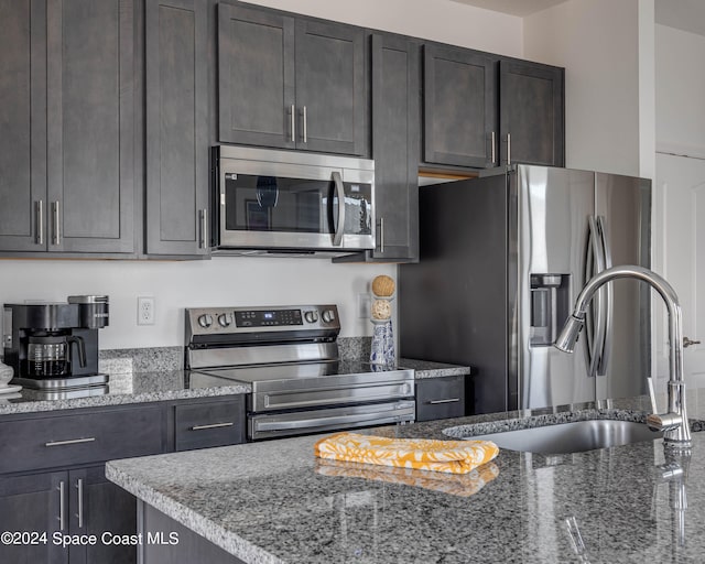 kitchen with dark brown cabinetry, appliances with stainless steel finishes, sink, and light stone counters