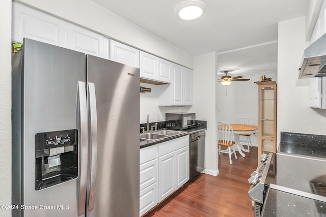 kitchen featuring dark wood-style flooring, dark countertops, a sink, stainless steel appliances, and white cabinetry