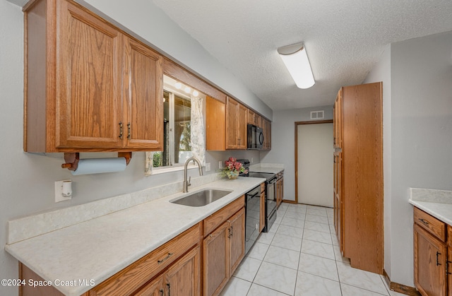 kitchen featuring a textured ceiling, black appliances, sink, and light tile patterned floors