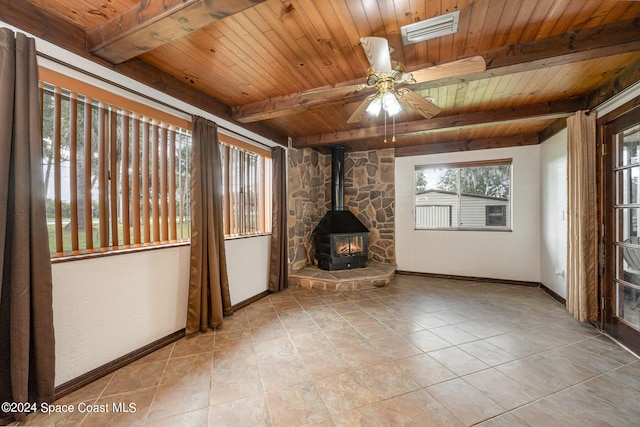 unfurnished living room with wood ceiling, a wood stove, light tile patterned floors, ceiling fan, and beam ceiling