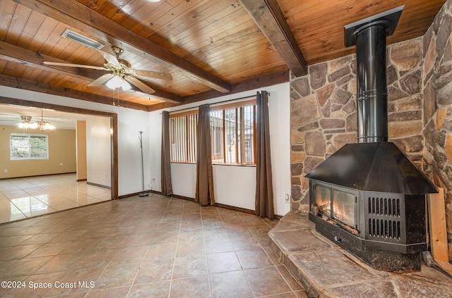 unfurnished living room featuring beamed ceiling, wood ceiling, a wood stove, and plenty of natural light