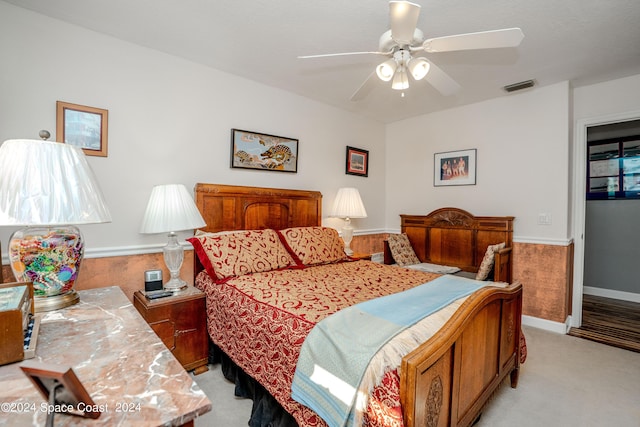 bedroom with wainscoting, ceiling fan, visible vents, and light carpet