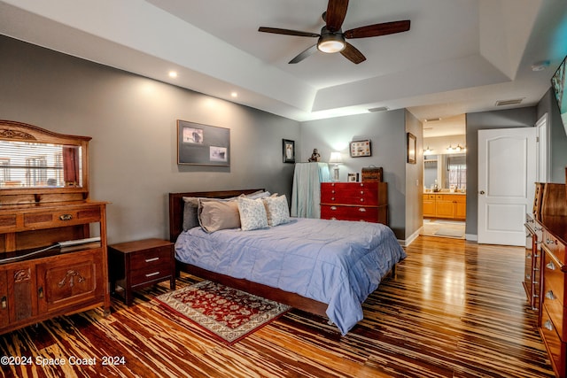 bedroom featuring a raised ceiling, hardwood / wood-style floors, ensuite bathroom, and ceiling fan