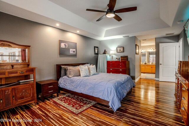 bedroom with connected bathroom, recessed lighting, wood finished floors, a tray ceiling, and visible vents