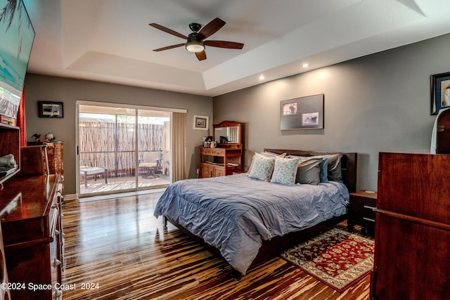 bedroom with ceiling fan, a raised ceiling, hardwood / wood-style floors, and access to exterior