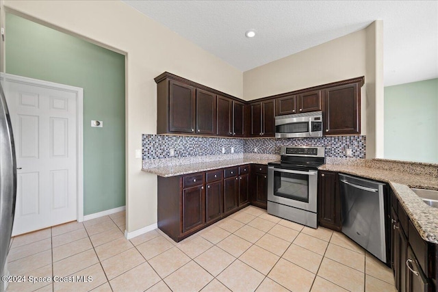 kitchen featuring decorative backsplash, light stone countertops, dark brown cabinetry, and stainless steel appliances