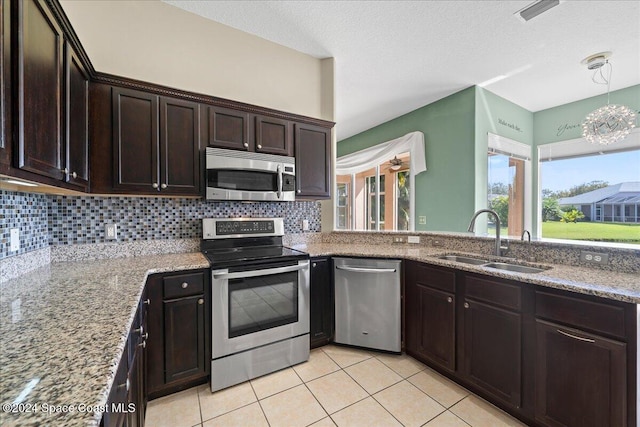 kitchen with appliances with stainless steel finishes, light tile patterned flooring, sink, dark brown cabinets, and light stone counters