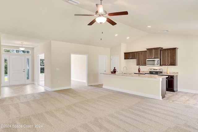 kitchen with stainless steel appliances, an island with sink, lofted ceiling, and light carpet