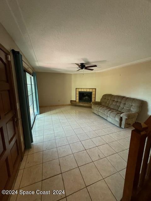 unfurnished living room with a fireplace, ceiling fan, light tile patterned floors, and a textured ceiling