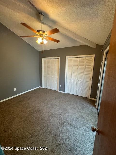 unfurnished bedroom featuring ceiling fan, a textured ceiling, carpet floors, and two closets