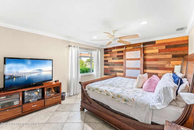 tiled bedroom featuring ceiling fan, wood walls, a textured ceiling, crown molding, and a barn door