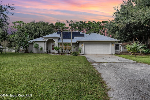 single story home with solar panels, a yard, and a garage