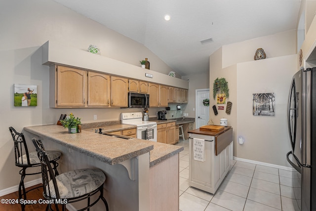 kitchen featuring kitchen peninsula, a breakfast bar, vaulted ceiling, light tile patterned floors, and appliances with stainless steel finishes