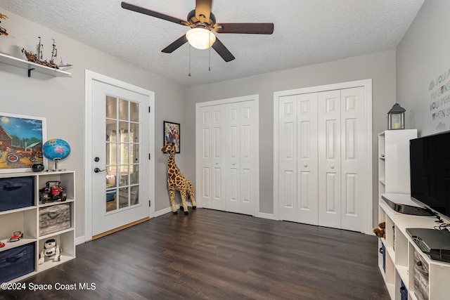 bedroom featuring dark wood-type flooring, two closets, a textured ceiling, and ceiling fan