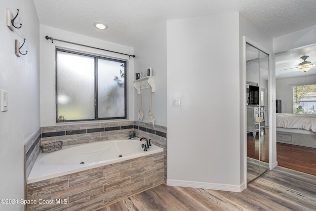 bathroom with ceiling fan, wood-type flooring, a textured ceiling, and tiled tub