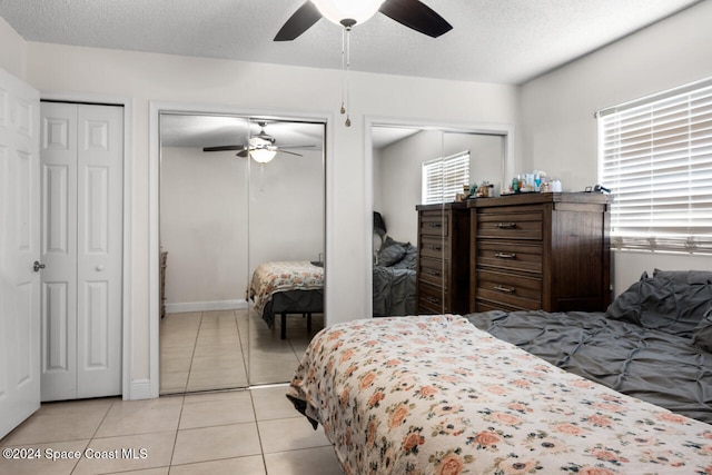 bedroom with a textured ceiling, two closets, light tile patterned floors, and ceiling fan