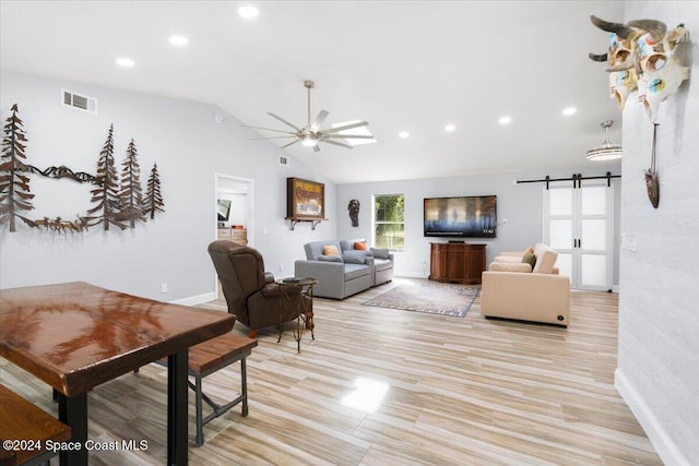 living room featuring light hardwood / wood-style floors, lofted ceiling, a barn door, and ceiling fan