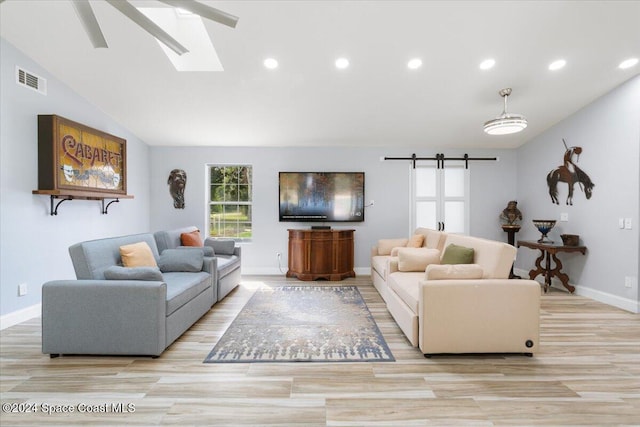 living room with ceiling fan, vaulted ceiling with skylight, light hardwood / wood-style flooring, and a barn door