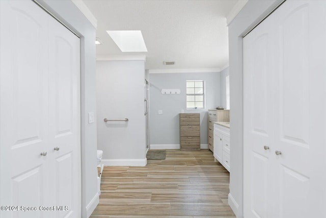 bathroom with ornamental molding, hardwood / wood-style floors, vanity, a textured ceiling, and a skylight