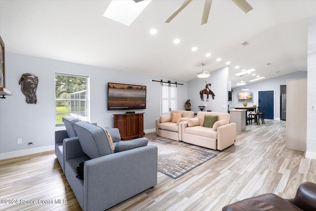 living room featuring vaulted ceiling with skylight, a barn door, light wood-type flooring, and ceiling fan