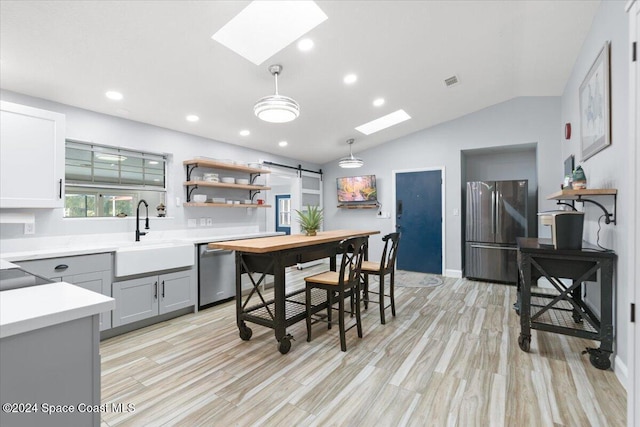 kitchen with gray cabinetry, sink, decorative light fixtures, lofted ceiling with skylight, and appliances with stainless steel finishes