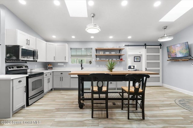 kitchen featuring stainless steel appliances, decorative light fixtures, a barn door, and white cabinets