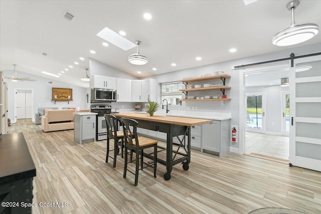 kitchen featuring a barn door, hanging light fixtures, lofted ceiling with skylight, range with electric stovetop, and light hardwood / wood-style flooring