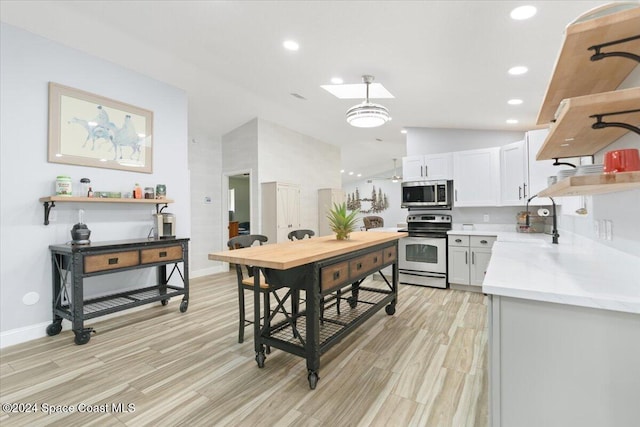 kitchen with vaulted ceiling, white cabinets, stainless steel appliances, and light hardwood / wood-style floors