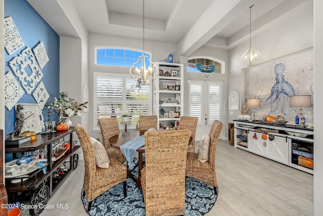 dining area with an inviting chandelier, light hardwood / wood-style flooring, a towering ceiling, and a tray ceiling