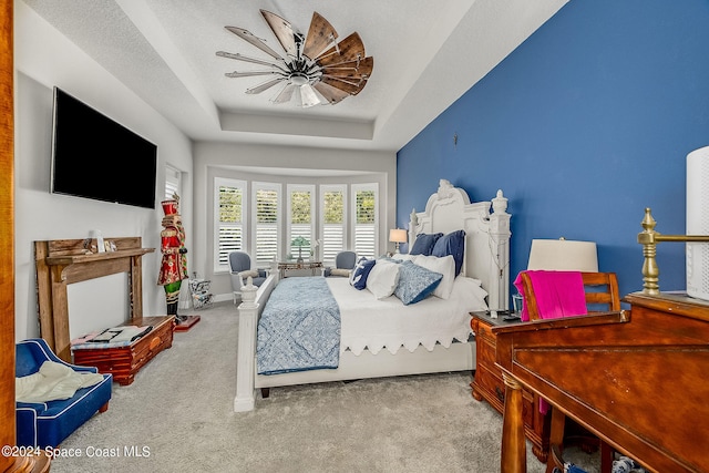 carpeted bedroom featuring a textured ceiling, ceiling fan, and a raised ceiling