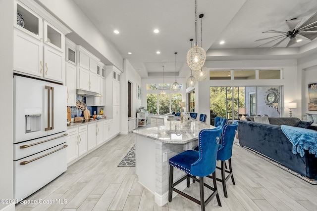 kitchen featuring light stone countertops, a kitchen island with sink, white fridge with ice dispenser, pendant lighting, and white cabinetry