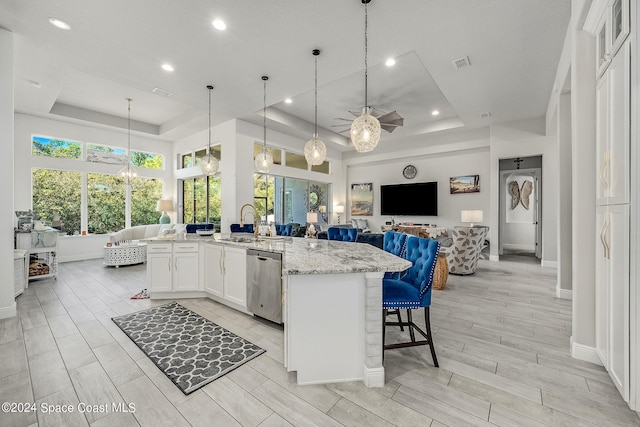 kitchen with a raised ceiling, white cabinetry, dishwasher, light stone countertops, and a kitchen bar