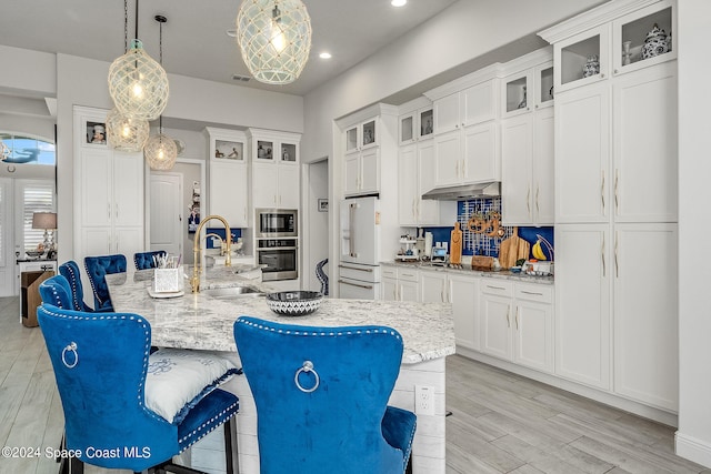 kitchen featuring hanging light fixtures, sink, a kitchen island with sink, appliances with stainless steel finishes, and light wood-type flooring