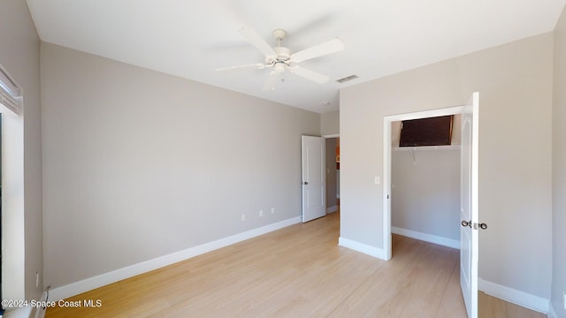 unfurnished bedroom with a closet, ceiling fan, light wood-type flooring, and a walk in closet