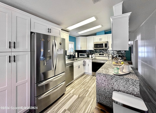 kitchen featuring lofted ceiling, appliances with stainless steel finishes, light stone counters, and white cabinetry