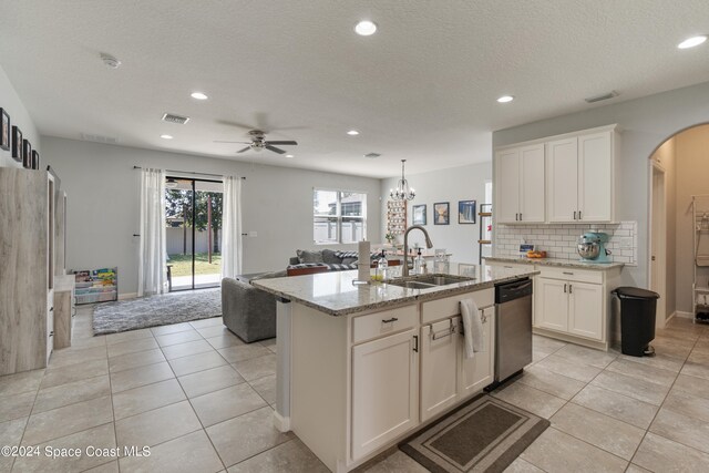 kitchen featuring an island with sink, white cabinetry, light stone countertops, dishwasher, and sink