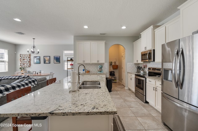 kitchen with stainless steel appliances, a center island with sink, sink, pendant lighting, and white cabinetry