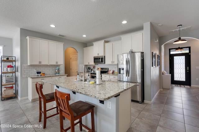 kitchen featuring stainless steel appliances, a kitchen island with sink, and white cabinets