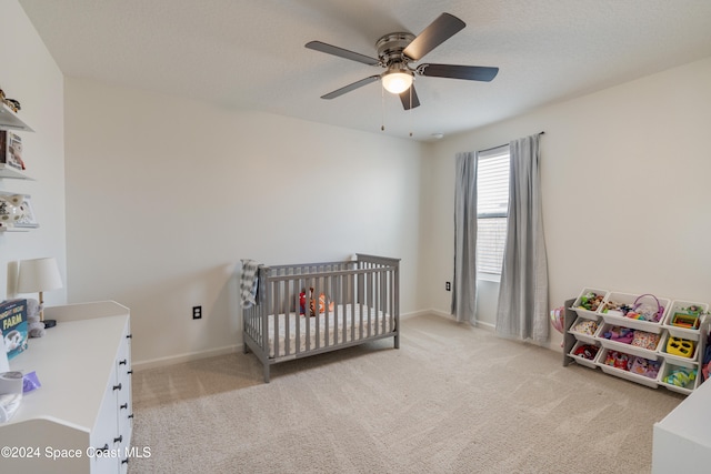 carpeted bedroom with a crib and ceiling fan