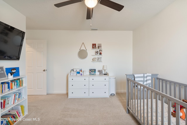 bedroom with ceiling fan, light carpet, and a nursery area