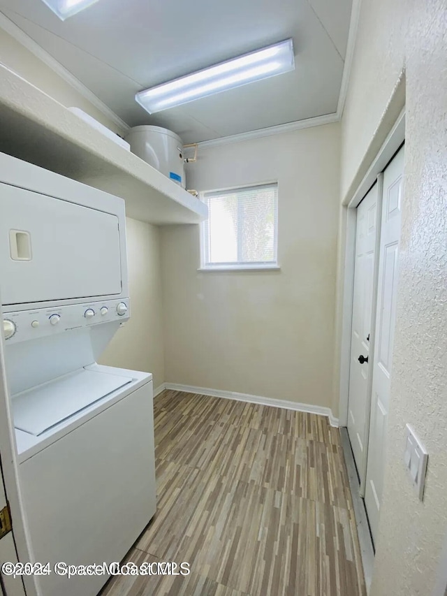 laundry area with light wood-type flooring, crown molding, and stacked washing maching and dryer