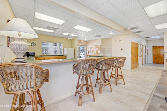 kitchen featuring a paneled ceiling, light hardwood / wood-style flooring, white fridge, a kitchen bar, and kitchen peninsula