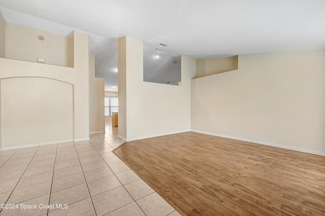 unfurnished room with a textured ceiling, high vaulted ceiling, and light hardwood / wood-style flooring