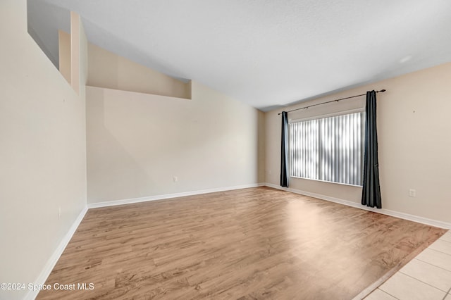 spare room with light hardwood / wood-style floors and vaulted ceiling