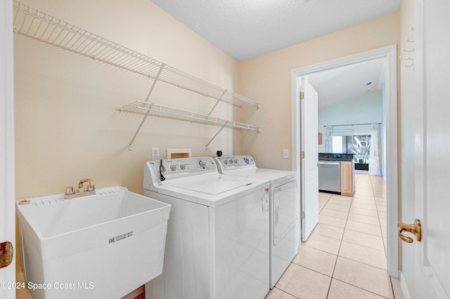 laundry area with a textured ceiling, light tile patterned floors, sink, and washing machine and clothes dryer