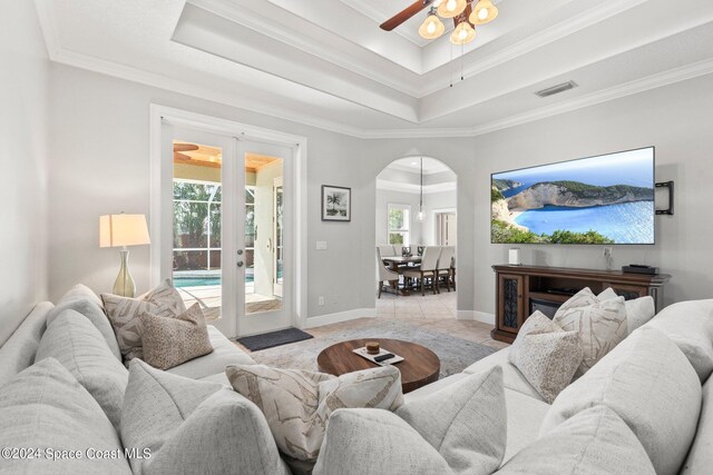 living room featuring a tray ceiling, ornamental molding, and light tile patterned floors